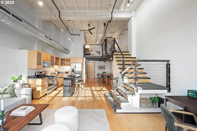 living room featuring ceiling fan, light hardwood / wood-style floors, a high ceiling, and sink