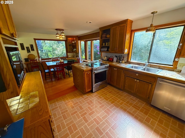 kitchen featuring a sink, brown cabinets, tile countertops, brick patterned floor, and appliances with stainless steel finishes