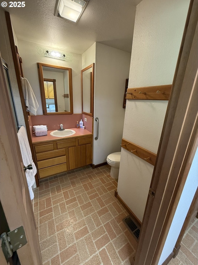 bathroom featuring brick patterned floor, a textured ceiling, toilet, visible vents, and vanity