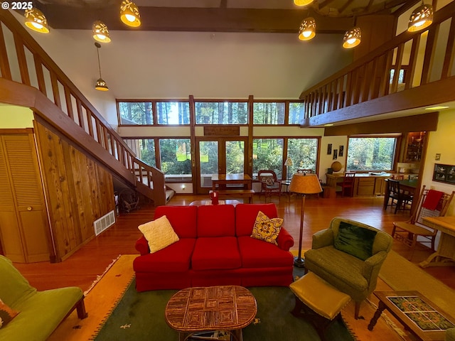 living room with visible vents, stairs, a towering ceiling, wood finished floors, and beamed ceiling