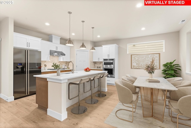 kitchen with an island with sink, appliances with stainless steel finishes, tasteful backsplash, decorative light fixtures, and white cabinetry