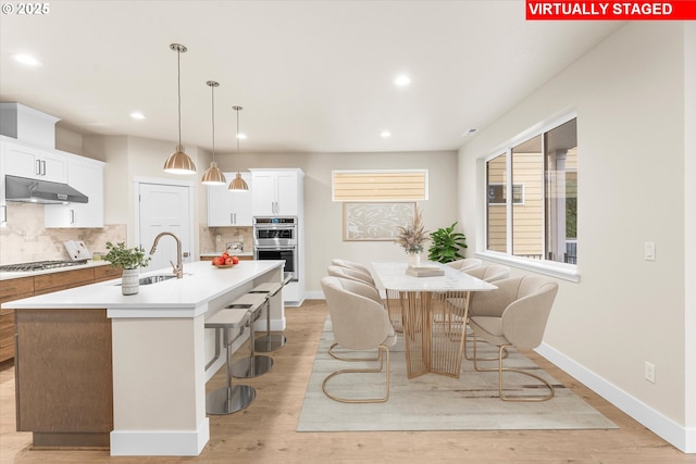 kitchen featuring white cabinetry, sink, backsplash, an island with sink, and decorative light fixtures