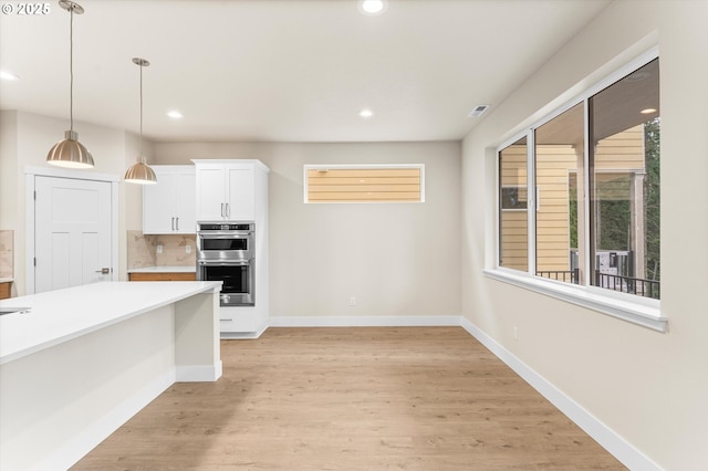 kitchen featuring decorative backsplash, stainless steel double oven, pendant lighting, white cabinets, and light hardwood / wood-style floors