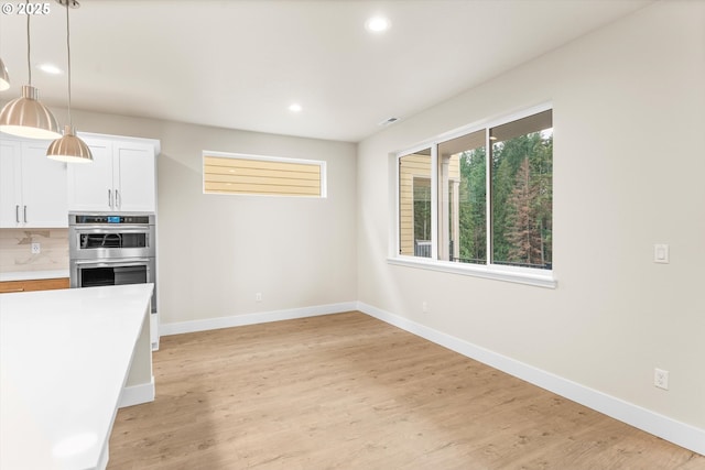 kitchen featuring decorative backsplash, double oven, pendant lighting, light hardwood / wood-style floors, and white cabinetry