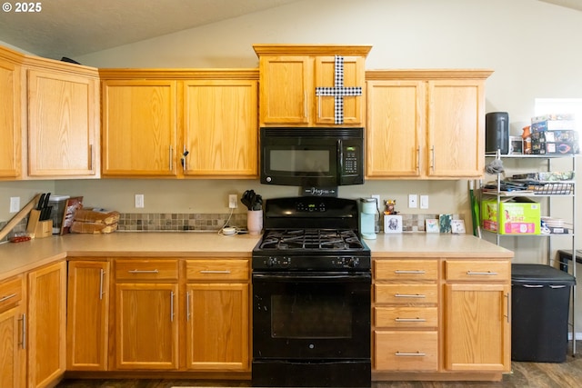 kitchen featuring lofted ceiling, black appliances, wood finished floors, and light countertops