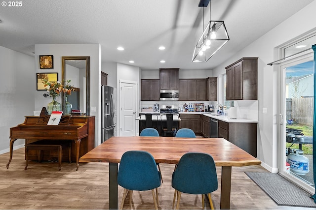 kitchen with dark brown cabinetry, sink, hanging light fixtures, stainless steel appliances, and light wood-type flooring