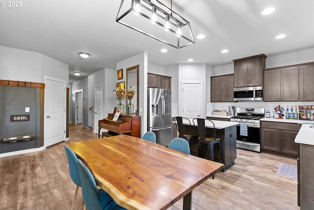 kitchen with dark brown cabinetry, stainless steel appliances, a textured ceiling, a center island, and light hardwood / wood-style floors