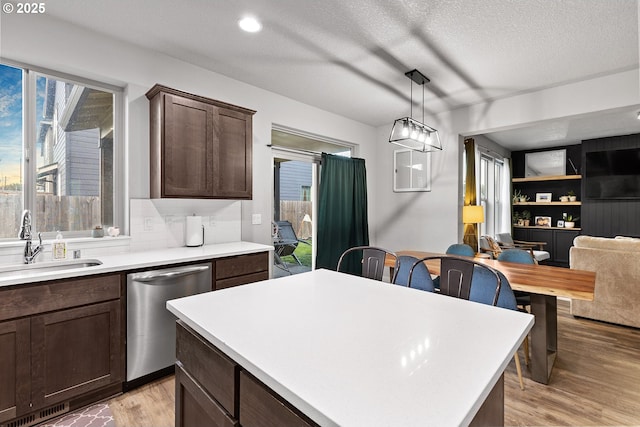 kitchen with stainless steel dishwasher, dark brown cabinetry, sink, decorative light fixtures, and light hardwood / wood-style floors