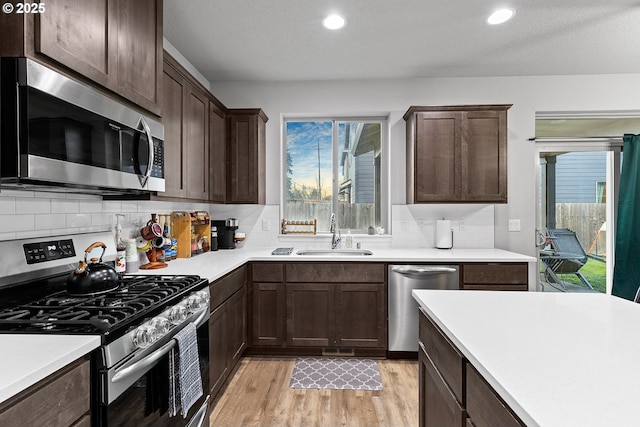 kitchen featuring appliances with stainless steel finishes, tasteful backsplash, a textured ceiling, sink, and light hardwood / wood-style floors