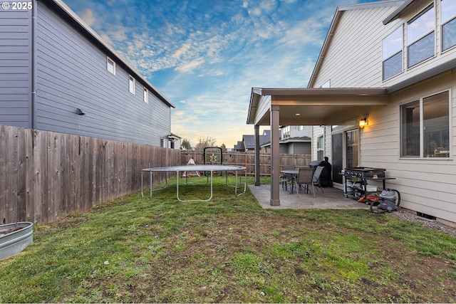 yard at dusk featuring a patio and a trampoline