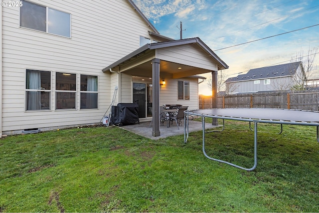 rear view of house with a trampoline, a patio area, and a lawn