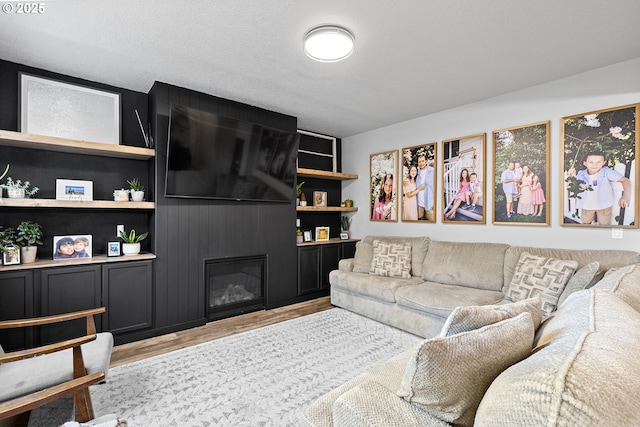 living room featuring a textured ceiling, built in shelves, a fireplace, and light hardwood / wood-style flooring