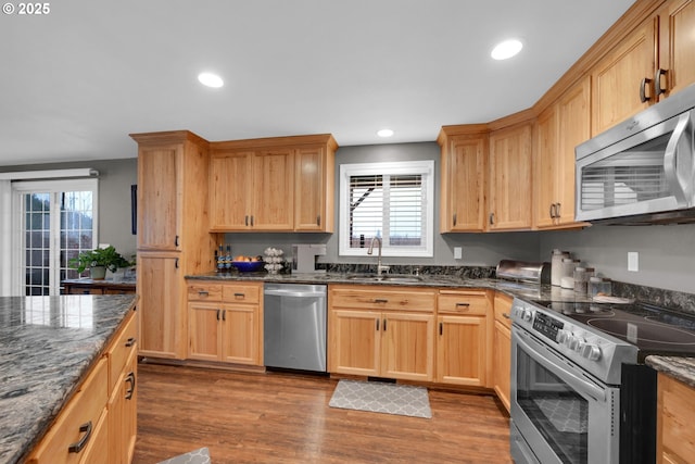 kitchen with recessed lighting, stainless steel appliances, a sink, dark wood-style floors, and dark stone countertops