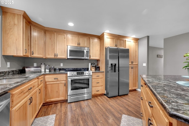 kitchen featuring dark stone countertops, dark wood-style flooring, stainless steel appliances, a sink, and recessed lighting