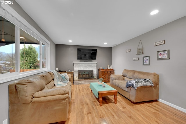 living room featuring light wood finished floors, a fireplace, baseboards, and recessed lighting