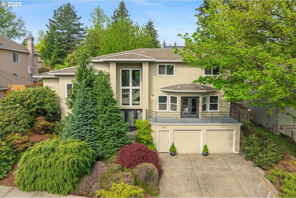 traditional-style house featuring a garage, a balcony, stucco siding, french doors, and driveway