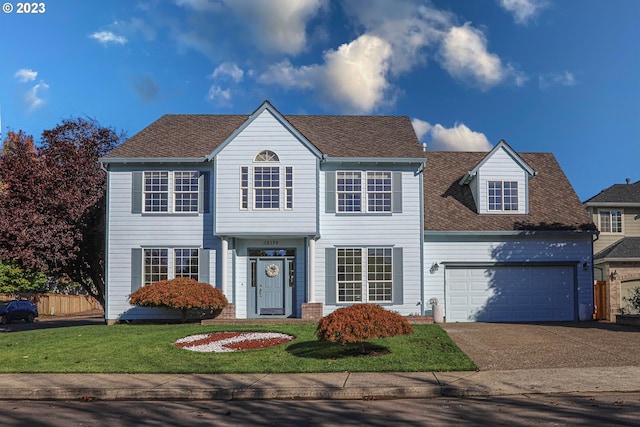 colonial inspired home featuring roof with shingles, a front yard, fence, a garage, and driveway