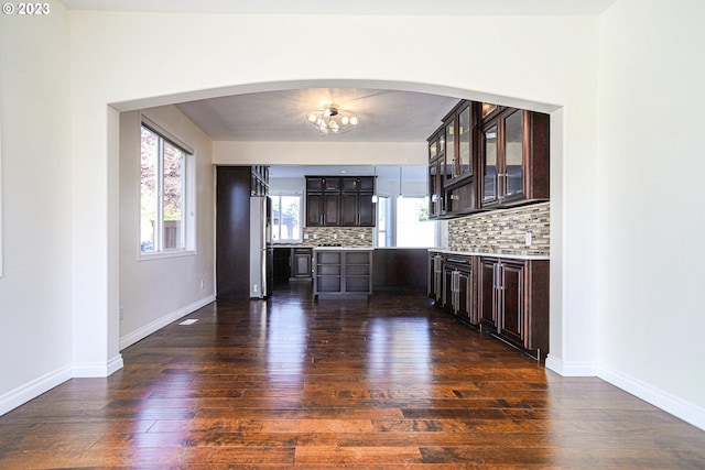 bar featuring arched walkways, dark wood-style flooring, baseboards, freestanding refrigerator, and decorative backsplash