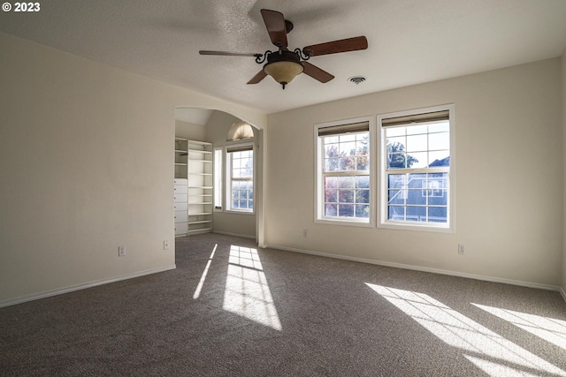 carpeted spare room featuring arched walkways, a textured ceiling, visible vents, a ceiling fan, and baseboards