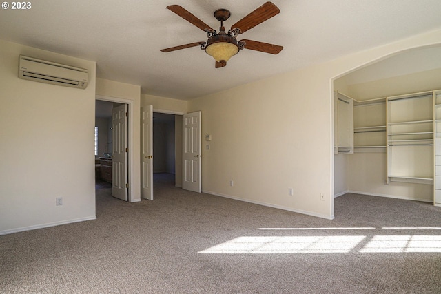 unfurnished bedroom with carpet floors, baseboards, a wall mounted AC, a closet, and a walk in closet