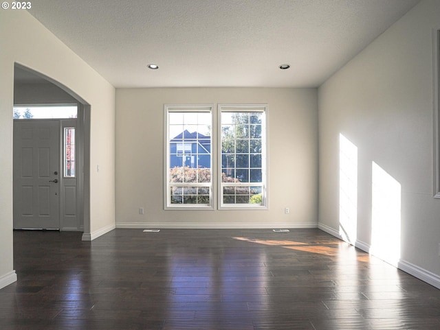 entrance foyer featuring arched walkways, dark wood-style flooring, and baseboards