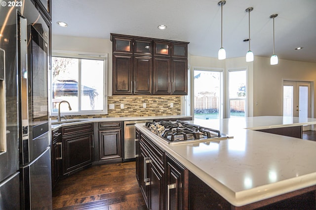 kitchen featuring dark wood-style floors, a center island, a sink, stainless steel appliances, and backsplash