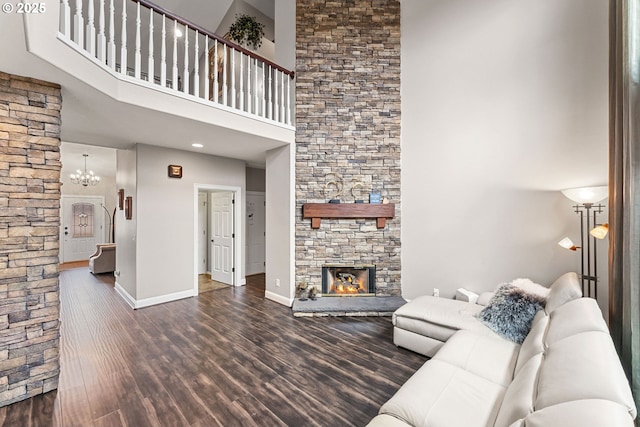 living room with an inviting chandelier, a towering ceiling, dark hardwood / wood-style floors, and a stone fireplace