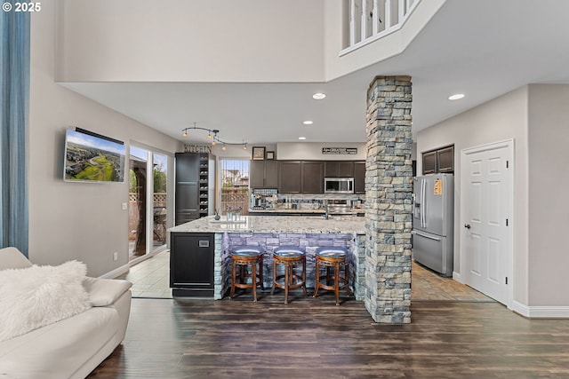 kitchen featuring ornate columns, backsplash, a kitchen breakfast bar, dark brown cabinetry, and stainless steel appliances