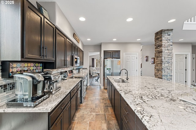 kitchen featuring sink, appliances with stainless steel finishes, dark brown cabinetry, light stone countertops, and ornate columns