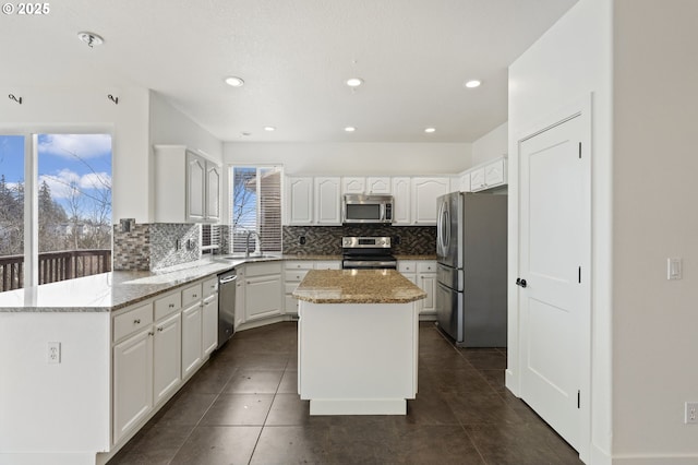 kitchen featuring a kitchen island, white cabinets, stainless steel appliances, light stone countertops, and backsplash