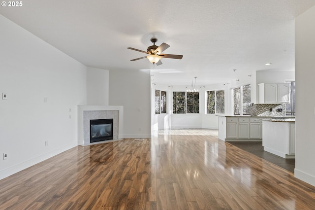 unfurnished living room with ceiling fan with notable chandelier, a fireplace, and dark hardwood / wood-style flooring