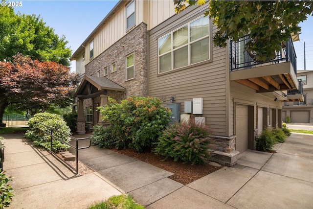608 NE Adwick Dr, Beaverton, OR 97006 - view of side of home with stone siding, a balcony, board and batten siding, a garage, and concrete driveway
