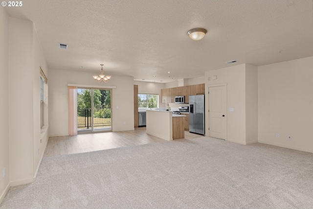608 NE Adwick Dr, Beaverton, OR 97006 - kitchen featuring appliances with stainless steel finishes, open floor plan, light colored carpet, a chandelier, and a kitchen island