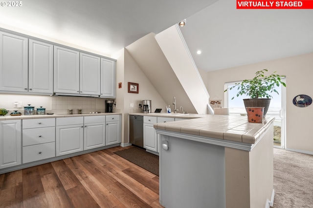 kitchen with hardwood / wood-style floors, tile counters, sink, kitchen peninsula, and stainless steel dishwasher