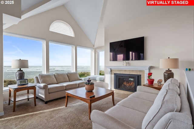 carpeted living room with high vaulted ceiling and a tiled fireplace