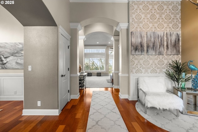 hallway featuring decorative columns, crown molding, and dark wood-type flooring