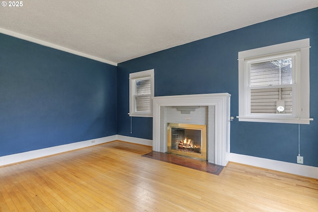 unfurnished living room featuring a fireplace, baseboards, wood-type flooring, and a textured ceiling