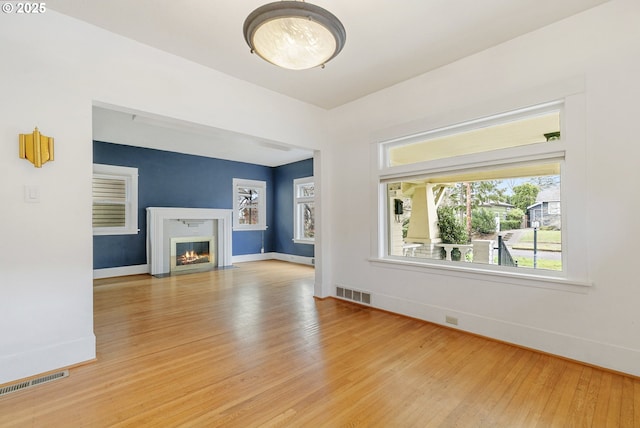 unfurnished living room with visible vents, a fireplace with flush hearth, baseboards, and light wood-style flooring