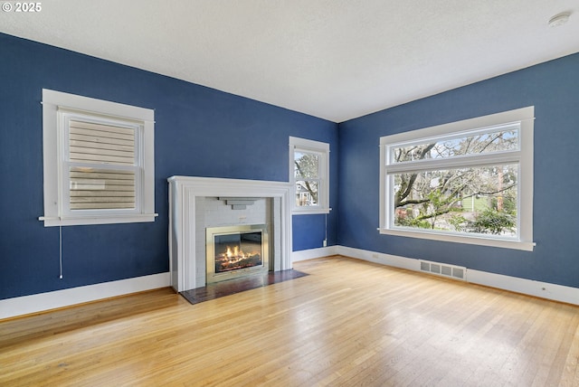 unfurnished living room featuring visible vents, a fireplace with flush hearth, baseboards, and hardwood / wood-style floors