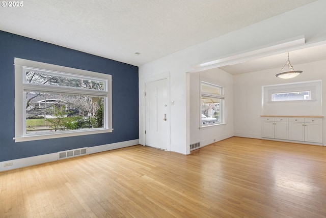 interior space with light wood-style flooring, baseboards, visible vents, and a textured ceiling