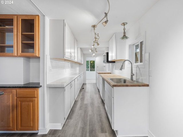 kitchen featuring pendant lighting, hardwood / wood-style floors, backsplash, sink, and white cabinetry