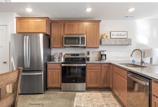 843 NE 11th St, Hermiston, OR 97838 - kitchen with stainless steel appliances, a sink, light stone counters, brown cabinets, and recessed lighting
