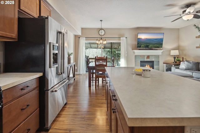 kitchen featuring high end fridge, hanging light fixtures, a center island, a fireplace, and wood-type flooring