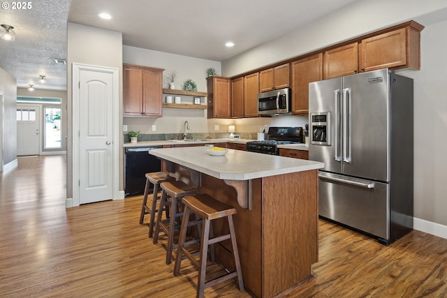 kitchen with sink, light hardwood / wood-style flooring, a breakfast bar area, a center island, and black appliances