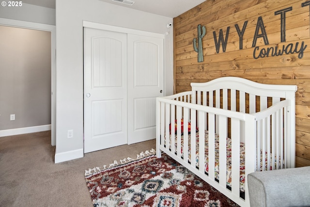 bedroom featuring dark colored carpet, wooden walls, a closet, and a crib