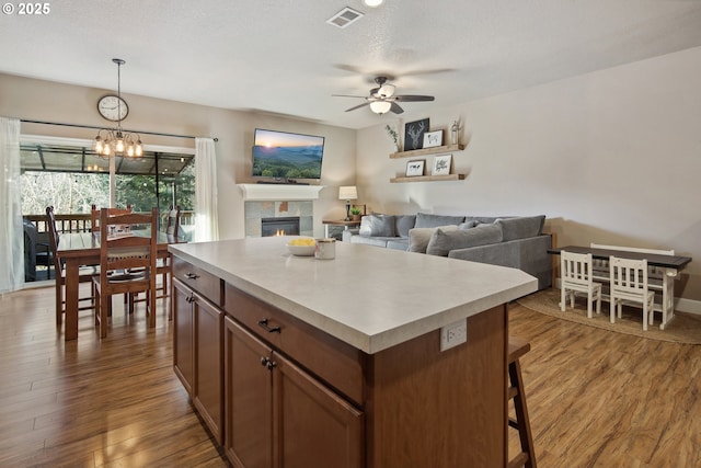 kitchen with pendant lighting, wood-type flooring, a textured ceiling, a kitchen island, and a tiled fireplace