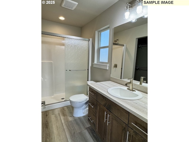 full bath with visible vents, a spacious closet, toilet, a stall shower, and wood finished floors