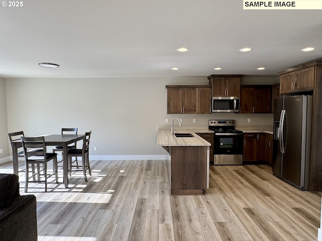 kitchen with appliances with stainless steel finishes, light wood-type flooring, a sink, and a peninsula