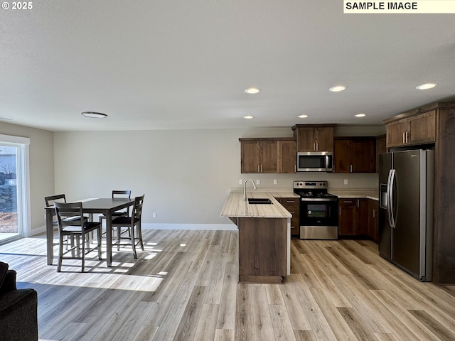 kitchen with light wood finished floors, appliances with stainless steel finishes, light countertops, and a sink