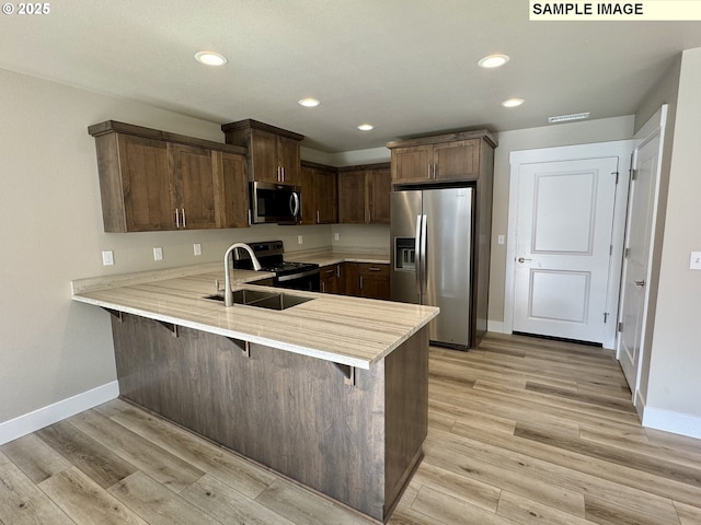 kitchen with a peninsula, light wood-style floors, light countertops, appliances with stainless steel finishes, and a kitchen bar